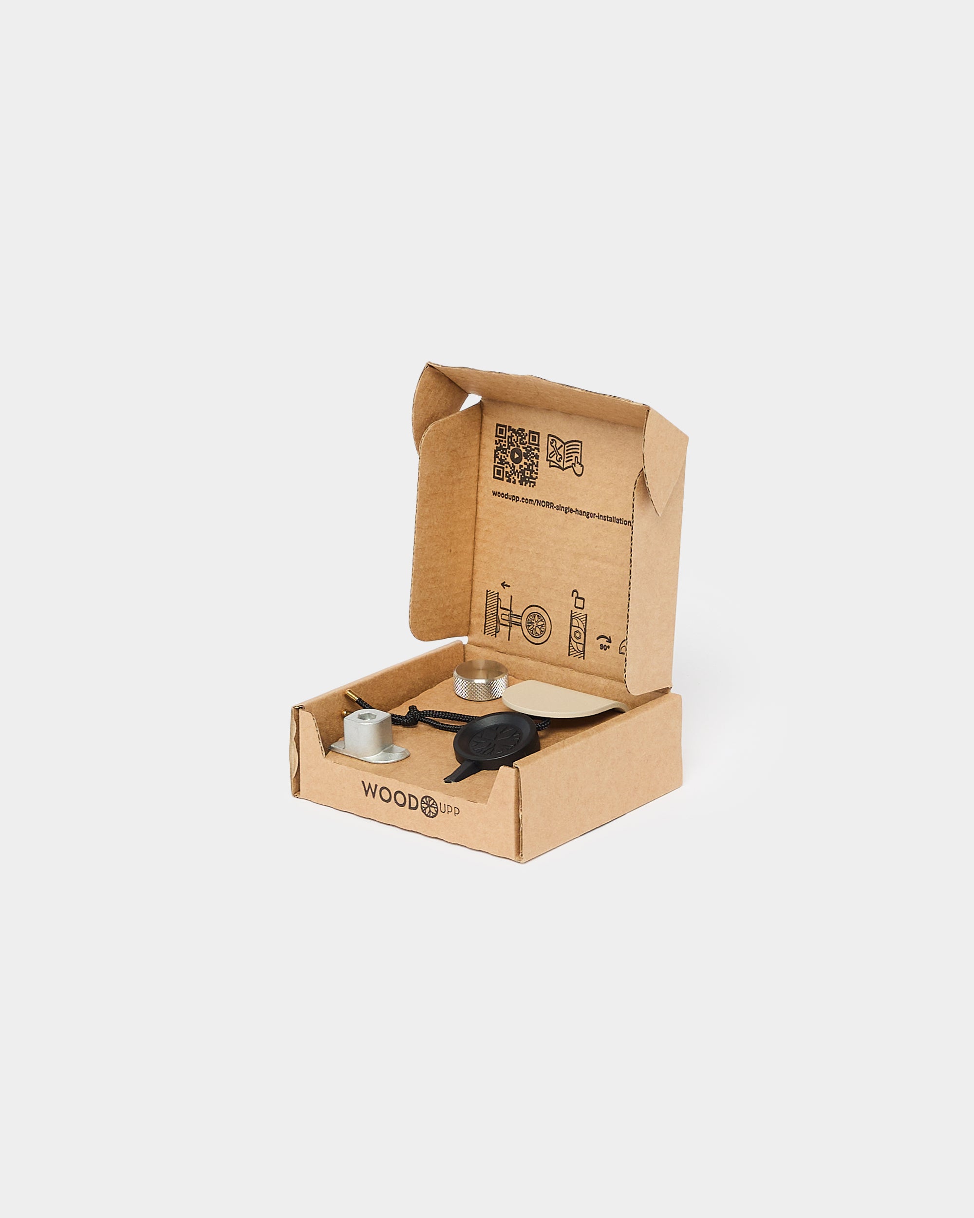 Open cardboard box labeled WOODD containing small metal and black mounting components for WoodUpp acoustic panels, shown on a plain white background.